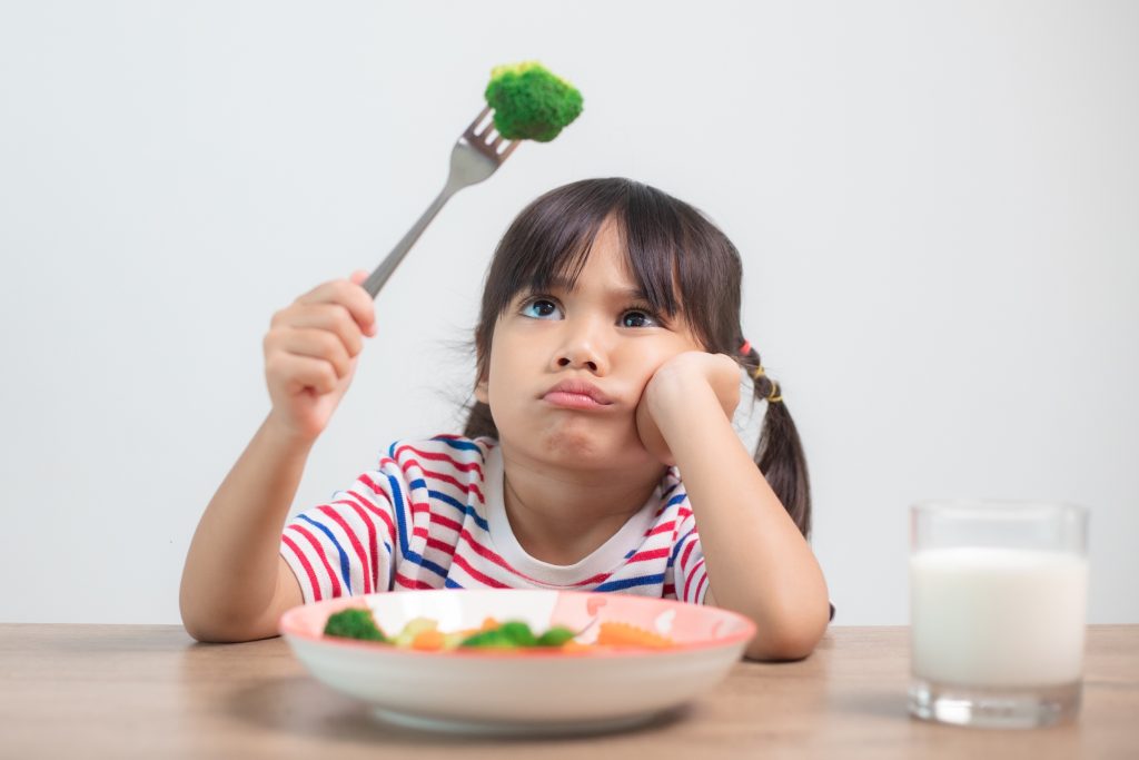 Child holding broccoli in the air looking at it confused.