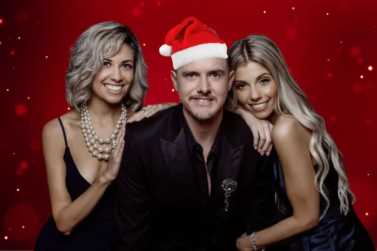 Two Brunettes and a Gay with red background and Aaron wearing a fake christmas hat