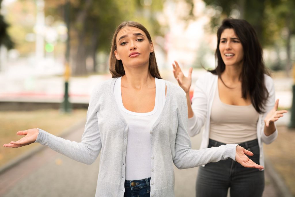 Two women, one looking unsure and one woman behind her looking confused about the friendship