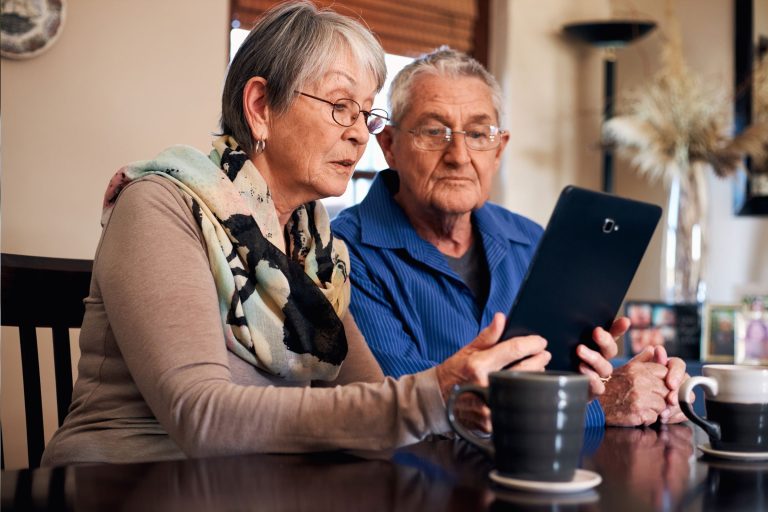 Retirees couple looking at an ipad in the dining room table