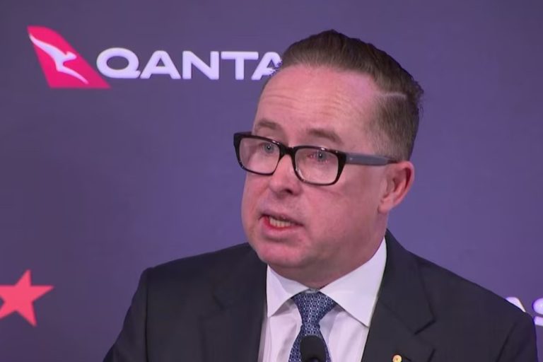 Alan Joyce sitting in front of the qantas and jetstar logos looking stressed