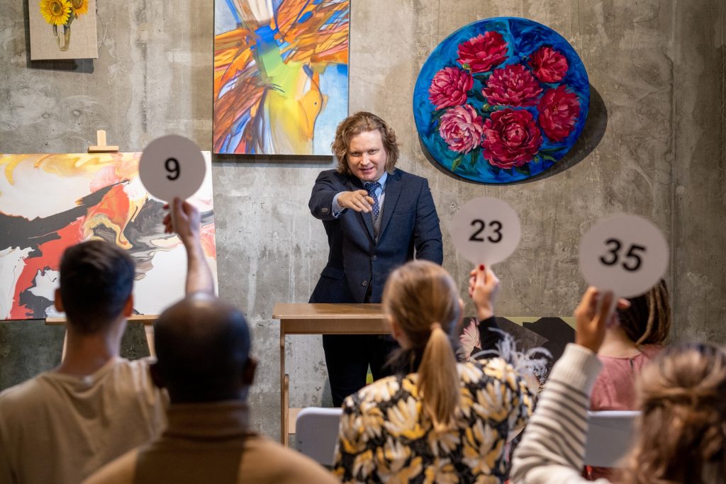 Auctioneering: An Auctioneer in front of patrons holding up bidding signs for a painting for sale