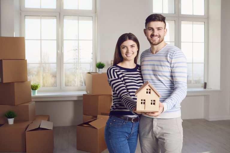 A female and a male standing inside tyheor new home folding a toy house together