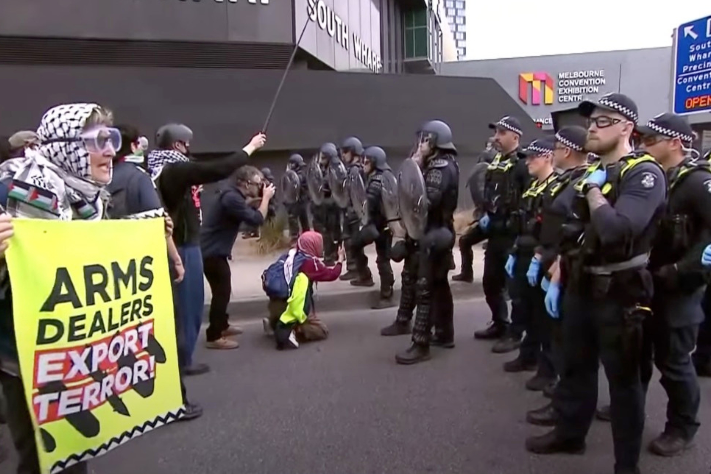 Riot police standing in front of protestors holding a sign