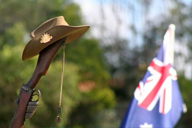 An Australian Flag in the distance with a Australian Defence Force Diggers Hat sitting onto of a rifle